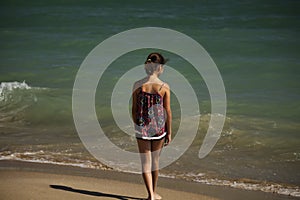 A pretty girl standing  on the beach and looking far into the sea, soft fockus