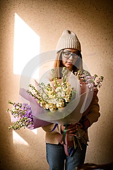 Pretty girl stands near a wall with a bouquet of lilac bushes