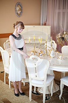 Pretty girl stands near white table with dishes