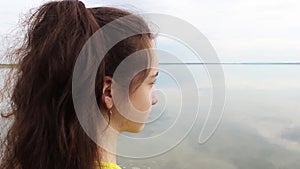 A pretty girl stands on the shore of the lake and squints at the bright light. Close-up of the back.