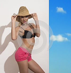 Pretty girl with staw hat, bra and shorts touches the hat