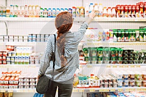 Pretty girl in striped shirt from back choosing dairy products in supermarket