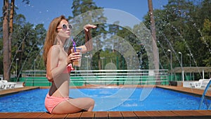 Pretty girl in sunglasses are sunbathing near pool