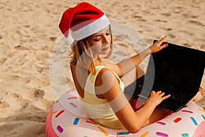 Pretty girl in a swimsuit and santa claus hats using laptop on the beach.