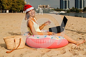 Pretty girl in a swimsuit and santa claus hats using laptop on the beach.