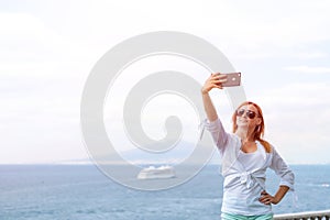 Pretty girl Takes a selfie photo. Sea and horizon in the background. Vacation and travel concept. Communication on a mobile