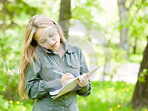 Pretty girl talking on the phone and writes in notebook