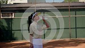 A pretty girl tennis player takes a break after training match. A young sportswoman stands sideways on the sports field