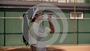 A pretty girl tennis player takes a break from workout or after training match. A young sportswoman stands sideways on