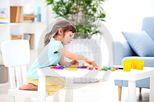 A pretty girl of three years old sits at the table and sculpts figures from colored clay. Sculpting and children`s creativity