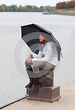 Pretty girl with umbrella sitting on the dock