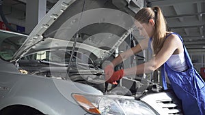 Pretty girl in uniform turns a screwdriver in a car engine. Car service, repair, maintenance and people concept -