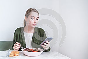 pretty girl uses a smearphone while eating at the restaurant. A woman eats a salad and looks at a smartphone