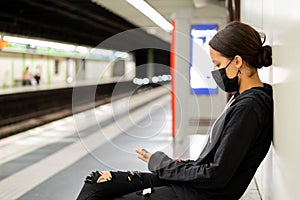 Pretty girl using her mobile phone while waiting for the train in the underground railway. Blurred background and copy space for