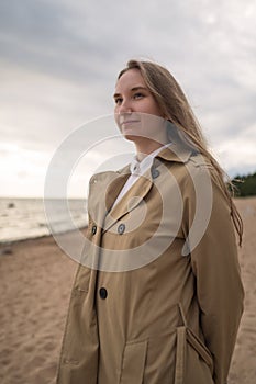 Pretty girl walking on a beach in beige trench coat