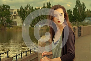 Pretty girl wearing black shirt, standing against fence by Volga River in Astrakhan in summer, looking back, filtered