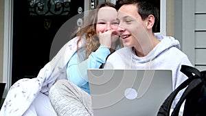 Pretty girl whispering secret in ear of her laughing friend in the hands of a computer sit on porch cover yourself with