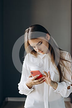 A pretty girl in a white blouse holds a smartphone.