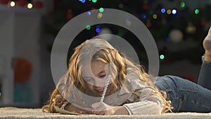 Pretty girl writing letter to Santa, closing her eyes with hands to image gifts