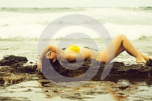 Pretty girl in yellow swimsuit lying on rocks on beach