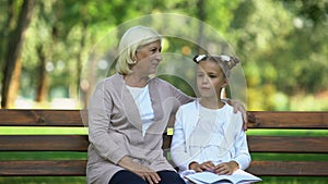 Pretty granny hugging little granddaughter listening her stories, female gossip