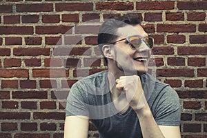 Pretty handsome young man hipster with sunglasses smiling laughing behind wooden wall. Looking aside. Toning.