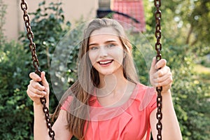 Pretty happy brunette swinging smiling near house in park on a sunny day.