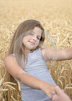 A pretty happy girl Holding the mother`s hands in golden wheat field. Concept of purity, growth, happiness