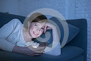 Pretty and happy red hair woman on her 20s or 30s lying on home couch or bed using mobile phone late at night smiling in internet