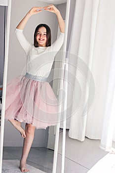 Pretty happy tween girl dancing like ballerina looking at mirror at home.