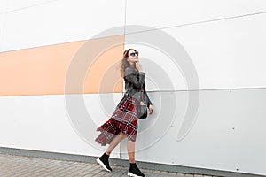 Pretty happy urban woman hipster in dark sunglasses with cute smile in fashionable youth red-black clothes and stylish sneakers