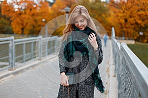 Pretty happy young woman in a vintage autumn stylish coat in a fashionable green scarf with a leather handbag is standing