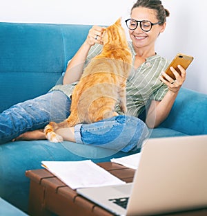 Pretty happy  young woman work home using laptop with her cat at sitting on the coach. Student freelancer lifestyle