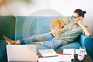 Pretty happy  young woman work home using laptop with her cat at sitting on the coach. Student freelancer lifestyle