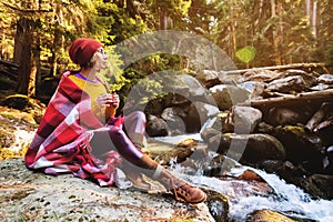 A pretty hipster girl with a plaid plaid on her shoulders in a hat and a yellow sweater and glasses with a mug of coffee