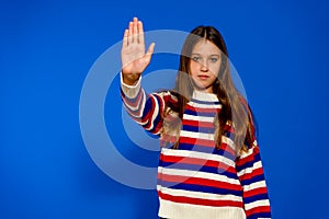 Pretty Hispanic girl making the gesture of stopping with the palm of her hand isolated on a blue studio background