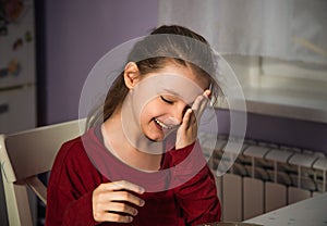 Pretty humor laughing kid girl hane the dinner on the home kitchen and holding the hand the head. Closeup