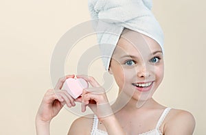 Pretty kid cleansing her face by heart shape pad. Portrait of beautiful little girl enjoying skincare procedures