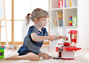 Pretty kid girl playing with a toy kitchen in children room