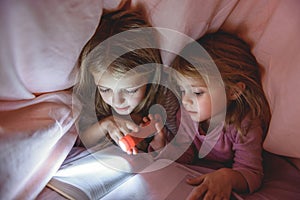 Pretty kids reading story under quilt