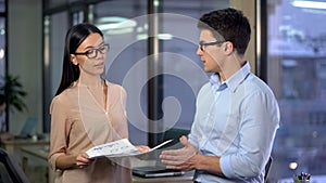 Pretty lady boss checking work of young trainee, viewing report of assistant