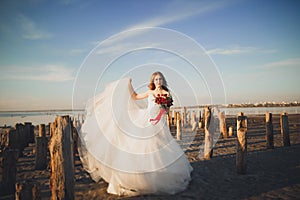 Pretty lady, bride posing in a wedding dress near sea on sunset