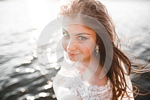 Pretty lady, bride posing in a wedding dress near sea on sunset