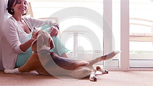 Pretty lady caressing his beagle dog while sitting on the floor of a well-lit room