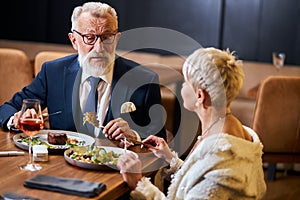 Pretty lady and elderly man having friendly conversation in restaurant