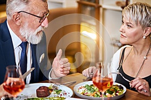 Pretty lady and elderly man having friendly conversation in restaurant