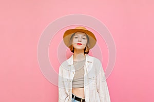 Pretty lady in hat and light summer clothes isolated on pink background, looking into camera with serious face. Portrait of