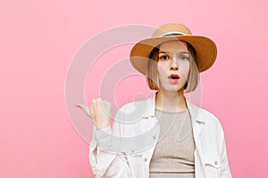 Pretty lady in hat with surprised face, looks into camera and shows thumb up on copy space isolated on pastel pink background.