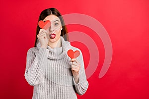 Pretty lady hiding eye little paper heart sticking tongue out mouth wear knitted pullover isolated red background