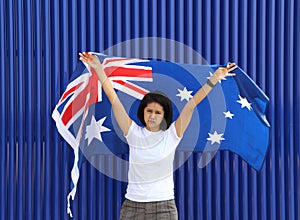 Pretty lady is holding Australia flag in her hands and raising to the end of the arm at the back